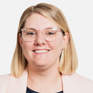 Frau mit blonden Haaren und heller Kleidung, neutraler Hintergrund.